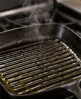 Ochucená litinová grilovací pánev se jemně zahřívá s velmi tenkým leskem oleje po vroubcích