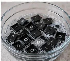 Black mechanical keyboard keycaps soaking in a bowl of warm soapy water.