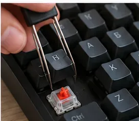 A keycap puller lifting a black keycap straight up from a mechanical switch.