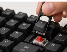 A hand lifting another black keycap from a red mechanical switch with a keycap puller.