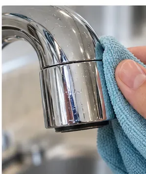 A soft microfiber cloth wiping water droplets from the finished surface of a sink faucet.