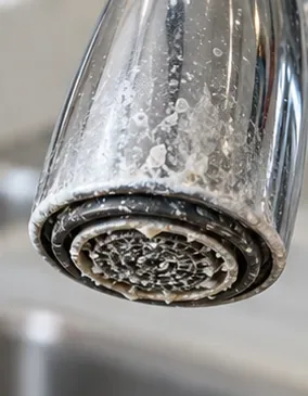 Close-up of a sink faucet aerator covered with white mineral deposits around the outlet.