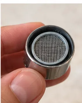 A cleaned faucet aerator held close to the camera with its mesh and gasket seated evenly.