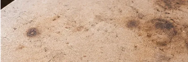 Detailní záběr na použitý kordieritový kámen na pizzu s několika hnědými a tmavými zapečenými skvrnami, ale bez silné kůrky od jídla.