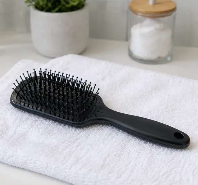 A clean black hairbrush rests on a white towel to air-dry after washing and disinfection.