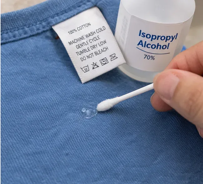 Vatový tampon nanáší malé množství 70% isopropylalkoholu k přilepení zbytků na modrou bavlněnou látku vedle štítku s pokyny pro péči
