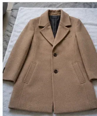 Beige uldfrakke lagt fladt på et hvidt håndklæde med omformede reverser og ærmer