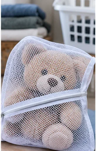 A tan teddy bear enclosed loosely inside a white mesh laundry bag