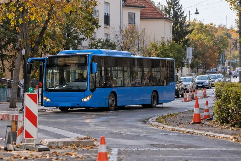 Plavi gradski autobus prolazi ulicom uz privremene narančaste čunjeve i zaštitnu prepreku.