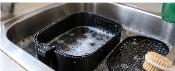 Airfryer-kurv og innsats som bløtlegges i varmt oppvaskvann i en vask