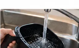 En svart airfryer-kurv skylles under rennende vann i vasken
