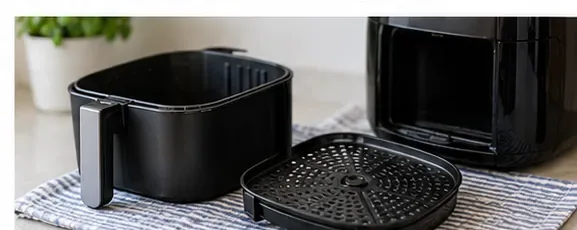 Rengjort airfryer-kurv og perforert innsats står på et kjøkkenhåndkle for å tørke