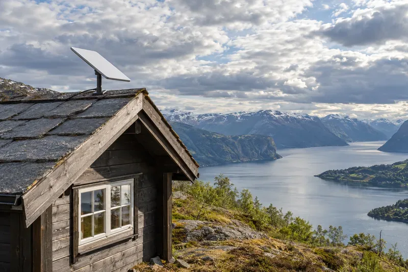 En hvit, flat satellittantenne på taket av en norsk hytte med åpen himmel over en fjord